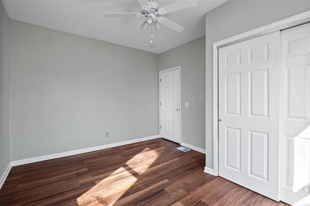 unfurnished bedroom with a closet, ceiling fan, dark wood-type flooring, and baseboards