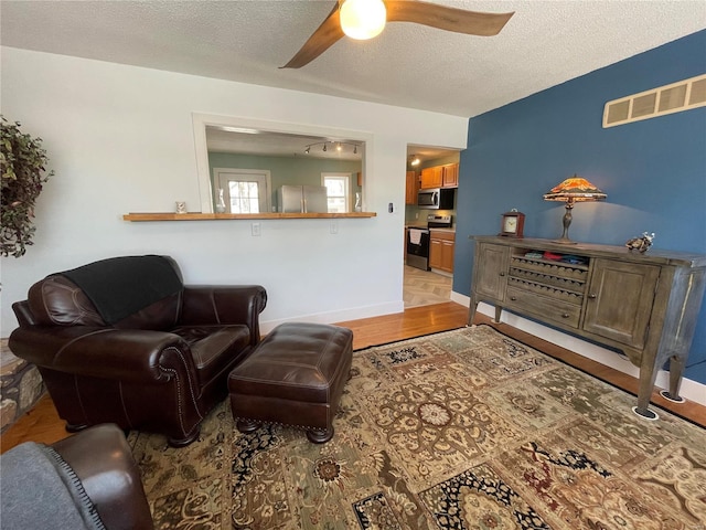 living room with a textured ceiling, ceiling fan, and light hardwood / wood-style flooring