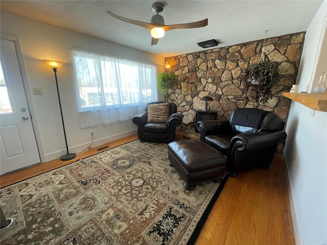 living room with a textured ceiling, ceiling fan, a wood stove, and hardwood / wood-style floors