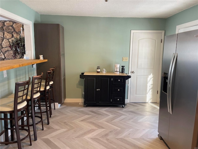 kitchen featuring butcher block countertops, a textured ceiling, light parquet floors, and stainless steel fridge with ice dispenser