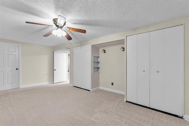 unfurnished bedroom featuring a textured ceiling, ceiling fan, light carpet, and multiple closets