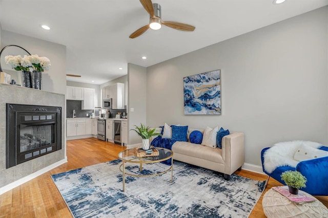 living room with a tiled fireplace, ceiling fan, light hardwood / wood-style flooring, and beverage cooler