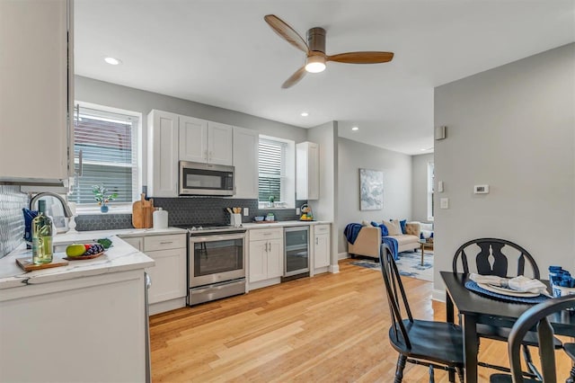 kitchen with backsplash, light wood-type flooring, appliances with stainless steel finishes, white cabinetry, and beverage cooler