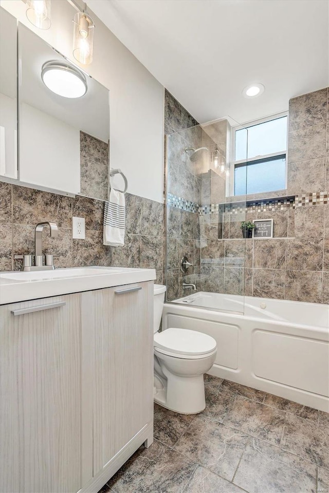 full bathroom featuring vanity, toilet, tiled shower / bath, and tile walls