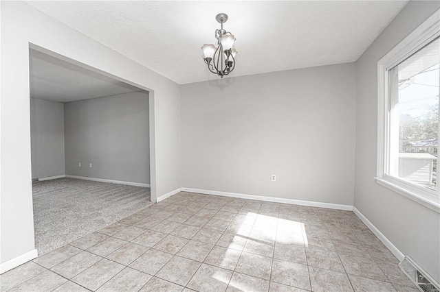 empty room featuring light tile patterned floors, a textured ceiling, and a chandelier