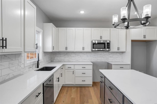 kitchen featuring sink, dishwasher, pendant lighting, light stone countertops, and white cabinets