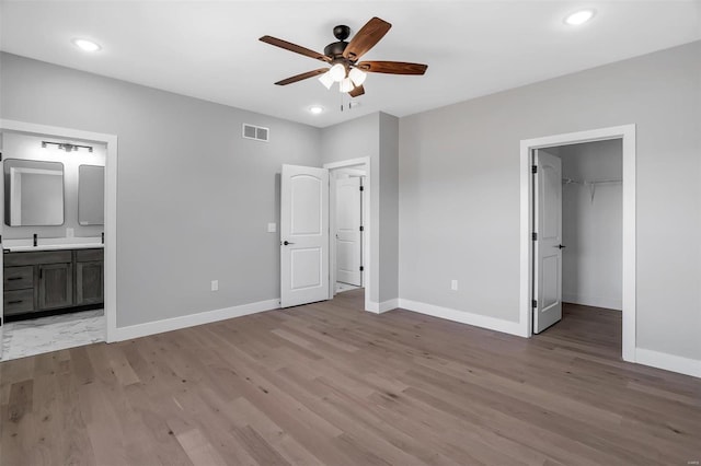 unfurnished bedroom with ensuite bathroom, a spacious closet, a closet, ceiling fan, and light hardwood / wood-style floors