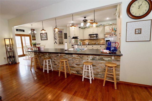 kitchen featuring appliances with stainless steel finishes, hardwood / wood-style floors, decorative light fixtures, a kitchen breakfast bar, and kitchen peninsula