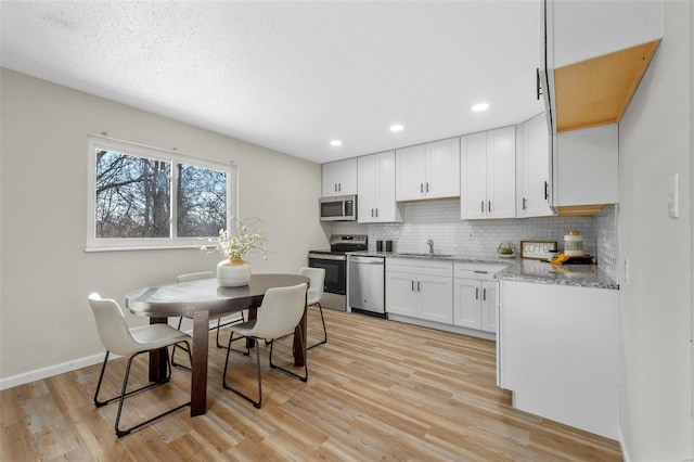 kitchen with tasteful backsplash, white cabinetry, sink, light hardwood / wood-style flooring, and stainless steel appliances