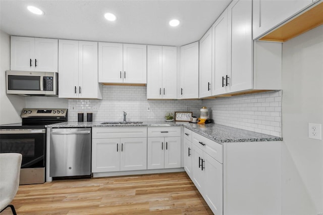 kitchen featuring light hardwood / wood-style floors, appliances with stainless steel finishes, white cabinets, sink, and backsplash