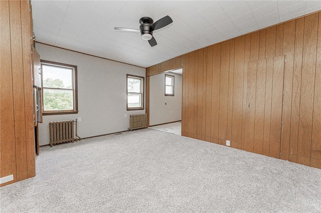 carpeted spare room with ceiling fan, wooden walls, and radiator