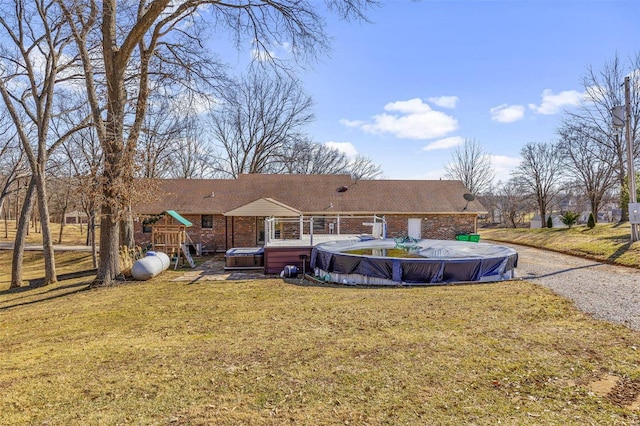 rear view of property with a swimming pool with hot tub, a yard, and a playground