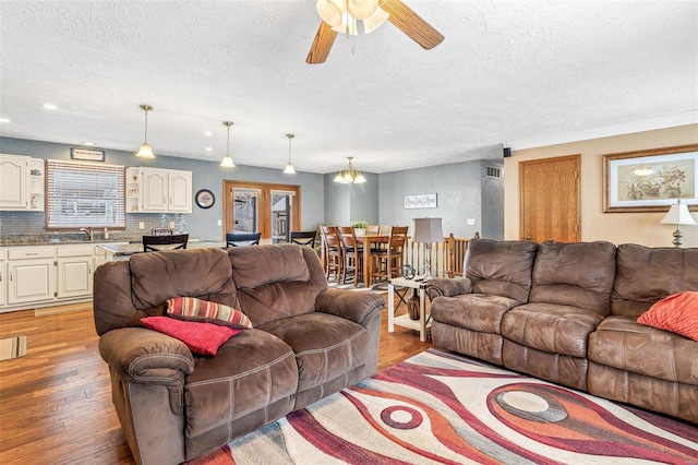 living room with ceiling fan, sink, light hardwood / wood-style floors, and a textured ceiling