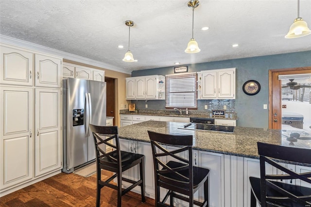 kitchen featuring sink, stainless steel fridge, a breakfast bar, dark stone countertops, and decorative light fixtures