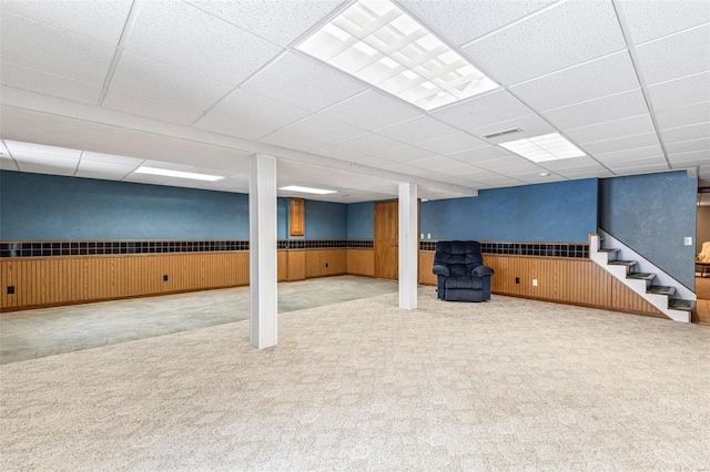 basement with light colored carpet, wooden walls, and a paneled ceiling