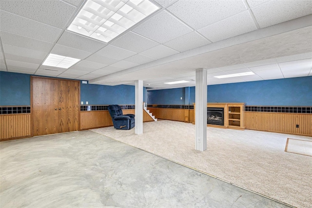 basement with carpet flooring, wooden walls, and a drop ceiling