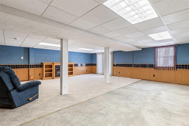 basement with carpet flooring, a paneled ceiling, and wood walls