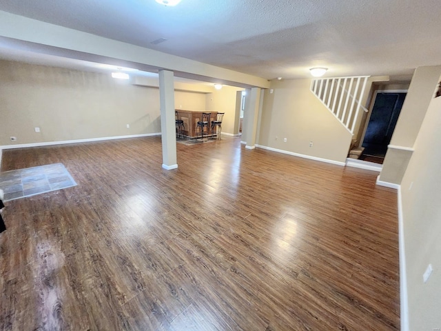 basement featuring wood-type flooring, a textured ceiling, and bar