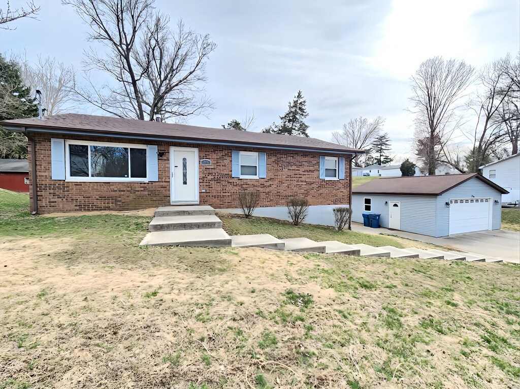 ranch-style home featuring brick siding, a detached garage, an outbuilding, and a front lawn
