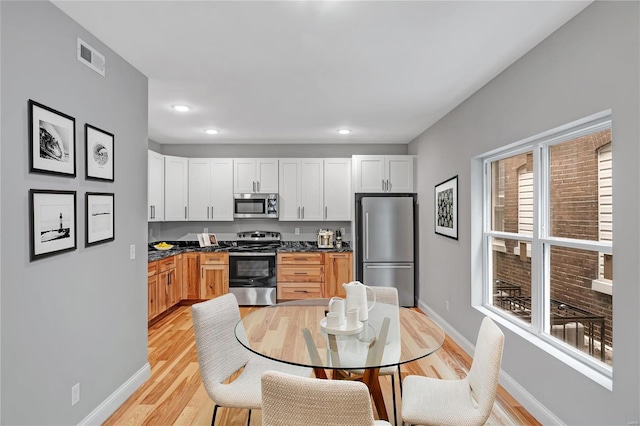 kitchen with light brown cabinets, white cabinets, stainless steel appliances, and light wood-type flooring