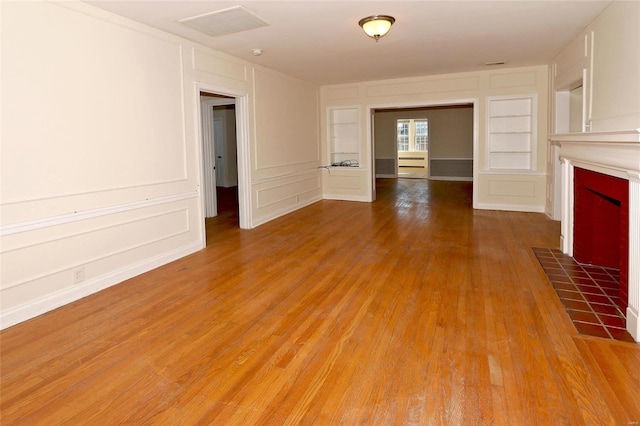 unfurnished living room featuring built in shelves, hardwood / wood-style floors, and a fireplace