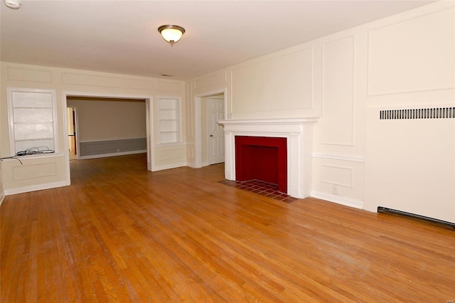 unfurnished living room featuring built in shelves, a tiled fireplace, and wood-type flooring