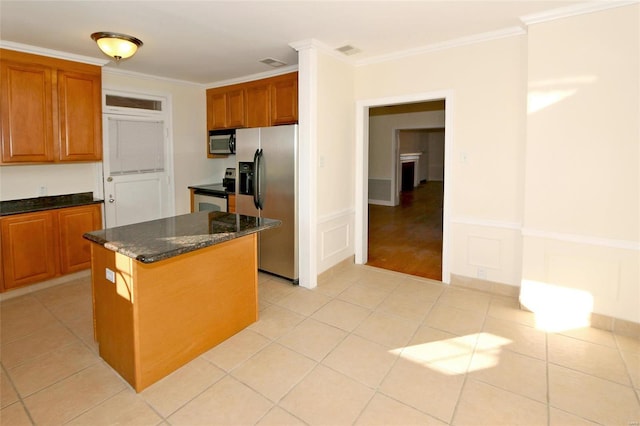 kitchen with appliances with stainless steel finishes, light tile patterned floors, a kitchen island, ornamental molding, and dark stone counters