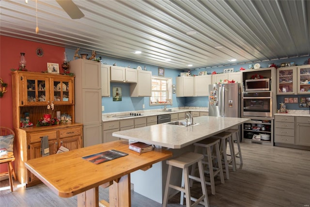 kitchen featuring dark wood-type flooring, a center island with sink, sink, appliances with stainless steel finishes, and a kitchen bar