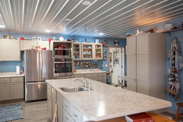 kitchen with appliances with stainless steel finishes, light wood-type flooring, a kitchen island with sink, and sink