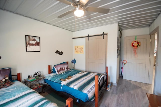 bedroom featuring a barn door, hardwood / wood-style flooring, and ceiling fan