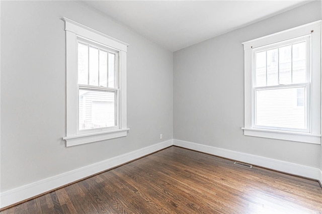 unfurnished room featuring baseboards, visible vents, and dark wood-type flooring