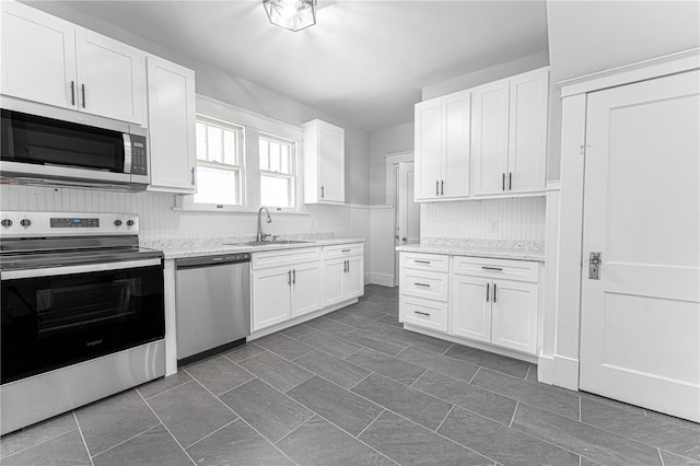 kitchen featuring light stone countertops, appliances with stainless steel finishes, white cabinets, and a sink