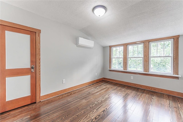 empty room featuring a wall mounted AC, vaulted ceiling, a textured ceiling, baseboards, and hardwood / wood-style flooring