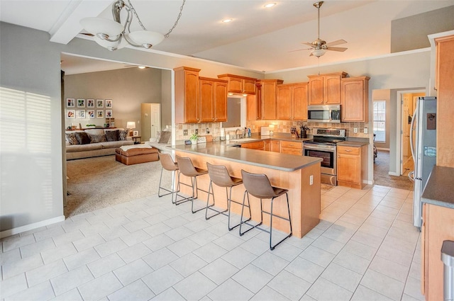 kitchen with tasteful backsplash, kitchen peninsula, a breakfast bar area, ceiling fan with notable chandelier, and appliances with stainless steel finishes