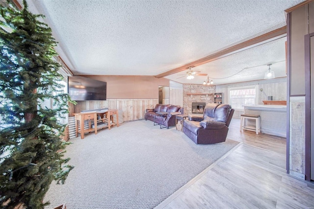 living room with ceiling fan, a textured ceiling, lofted ceiling with beams, and a stone fireplace