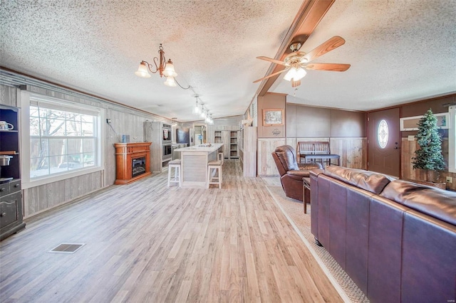 living room featuring rail lighting, wooden walls, a textured ceiling, ceiling fan with notable chandelier, and light hardwood / wood-style flooring