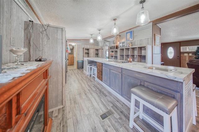 kitchen with light stone countertops, wooden walls, a textured ceiling, and pendant lighting