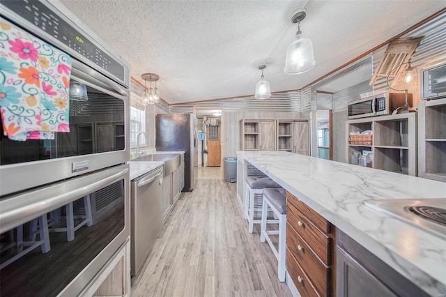 kitchen with light stone countertops, a textured ceiling, appliances with stainless steel finishes, hanging light fixtures, and ornamental molding