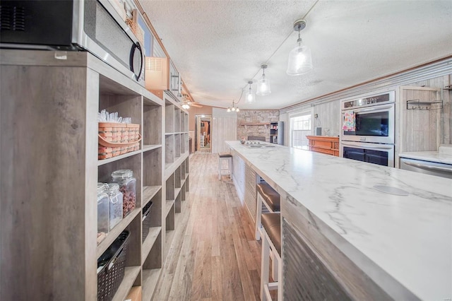 kitchen with light stone countertops, a textured ceiling, double oven, hanging light fixtures, and light hardwood / wood-style flooring