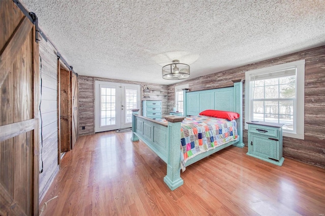 bedroom featuring light hardwood / wood-style floors, multiple windows, a barn door, and french doors