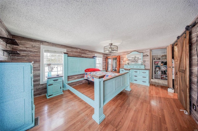 kitchen with a barn door, light hardwood / wood-style flooring, wooden walls, and a kitchen bar