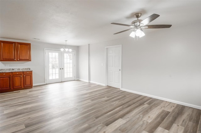 unfurnished living room featuring french doors, ceiling fan with notable chandelier, and light hardwood / wood-style flooring