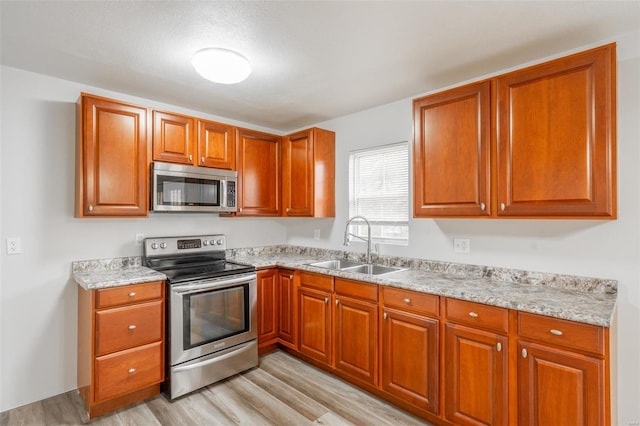 kitchen featuring light stone countertops, light wood-type flooring, sink, and appliances with stainless steel finishes