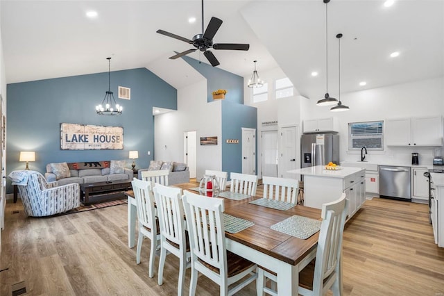 dining area with high vaulted ceiling, ceiling fan with notable chandelier, and light wood-type flooring