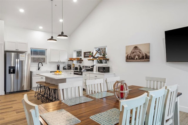 dining space featuring light wood-type flooring, high vaulted ceiling, and sink