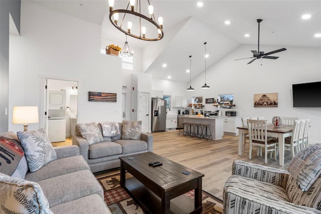 living room with ceiling fan with notable chandelier, high vaulted ceiling, and light hardwood / wood-style flooring