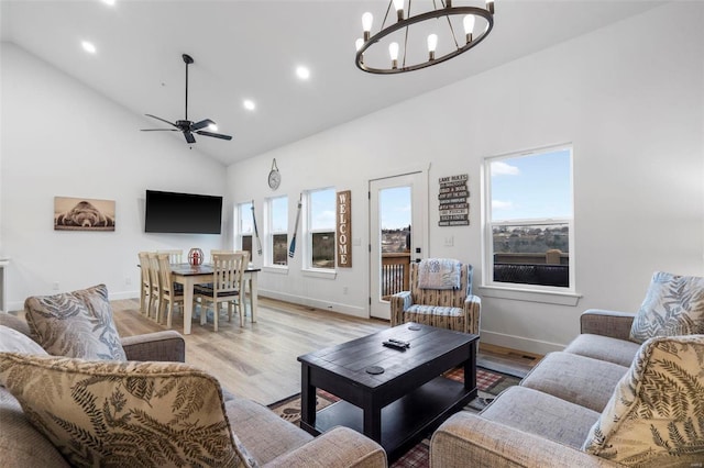 living room with ceiling fan with notable chandelier, light hardwood / wood-style flooring, and high vaulted ceiling