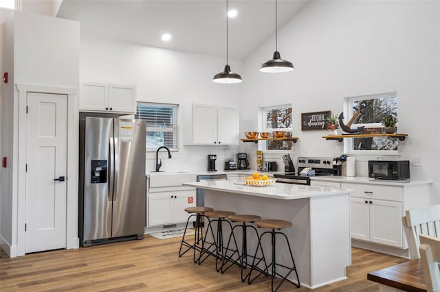 kitchen with white cabinetry, sink, high vaulted ceiling, a kitchen island, and appliances with stainless steel finishes