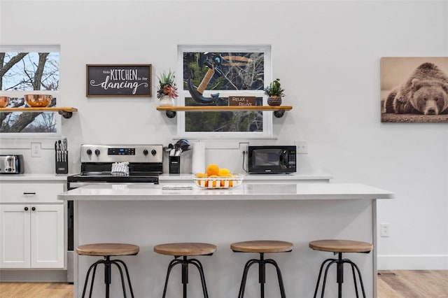 kitchen with a kitchen breakfast bar, light hardwood / wood-style floors, stainless steel electric range, and white cabinetry