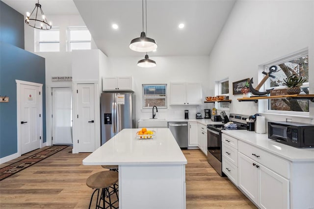 kitchen with a center island, a high ceiling, hanging light fixtures, white cabinetry, and stainless steel appliances